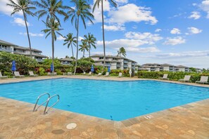 Una piscina con sillones de descanso y palmeras, rodeada de edificios de varios pisos.