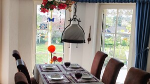 Comedor con mesa dispuesta para seis personas, sillas, lámpara colgante y vista a un jardín a través del ventanal.