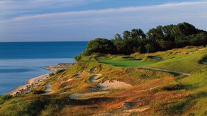 Ein Küsten-Golfplatz mit freiem Blick auf das Meer, einer gepflegten Spielbahn und einem bewaldeten Bereich.