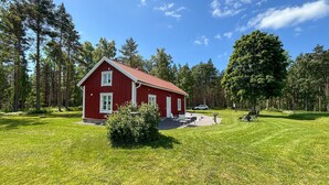 Een rode houten woning met een schuin dak, omgeven door een verzorgd gazon en hoge bomen.