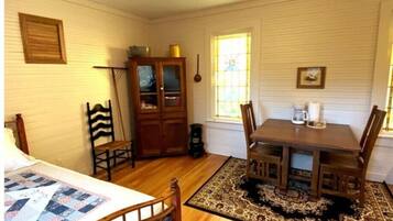 A room with a wooden dining table, chairs, a cabinet, and a quilt on the bed.