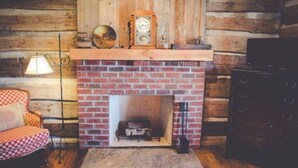 A cozy room with a brick fireplace, a wooden mantel, and a checkered armchair. - Audrey's Abode - Restored log cabin, country setting, minutes from Jacksonville
 (Jacksonville)