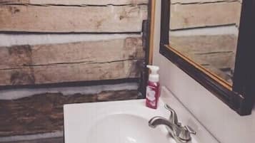 Un baño con pared de madera, un lavamanos blanco, un espejo, una toalla y un dispensador de jabón.