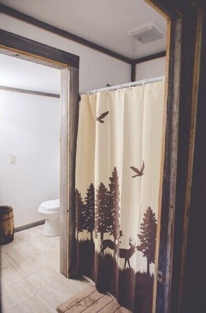 A bathroom with a shower curtain featuring a forest scene. - Audrey's Abode - Restored log cabin, country setting, minutes from Jacksonville
 (Jacksonville)