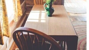 A wooden dining table with chairs, a vase with yellow flowers, and a hanging lamp in a rustic room with wooden walls and a window with curtains. - Audrey's Abode - Restored log cabin, country setting, minutes from Jacksonville
 (Jacksonville)