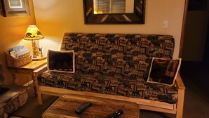 A cozy living room with a patterned sofa, two pillows, a lamp, and two remote controls on a wooden coffee table. - Hillcrest Suites & Cabins (Big Bear Lake)