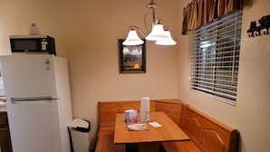 A compact kitchen with a refrigerator, microwave, and wooden bench. - Hillcrest Suites & Cabins (Big Bear Lake)