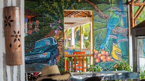 A vibrant mural with a car, tropical plants, and birds. - HOTEL PALMAS DE SANTA ELENA  (Quimbaya)