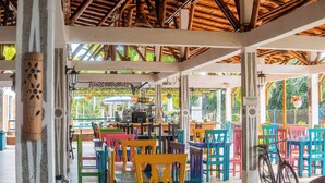 A covered outdoor seating area with colorful chairs and tables, a bicycle, and a view of the surrounding greenery. - HOTEL PALMAS DE SANTA ELENA  (Quimbaya)