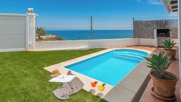 Une piscine avec vue sur la mer, une pelouse et quelques plantes en pot.