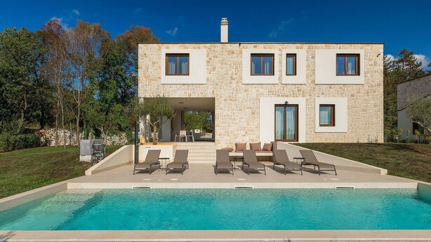 Une maison moderne à deux étages, dotée d’une façade en pierre, d’une piscine et d’un espace de détente extérieur.