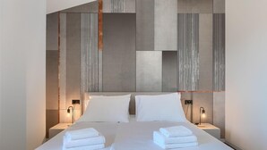 Une chambre d’hôtel moderne dotée d’un grand lit, de deux tables de chevet et d’un décor mural original aux textures variées.