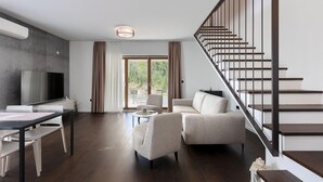 Un salon moderne doté d’un téléviseur à écran plat, d’un coin repas avec une table et des chaises, d’un canapé et d’un escalier avec une rampe.
