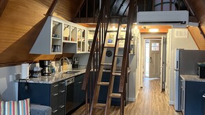 Una cucina in stile loft con soffitto in legno, pensili a incasso, isola centrale e scala che conduce a un livello superiore.