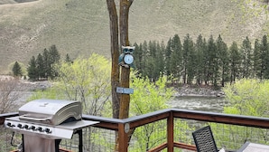 Una terrazza con barbecue e tavolo con sedie, affacciata su un fiume e colline boscose.