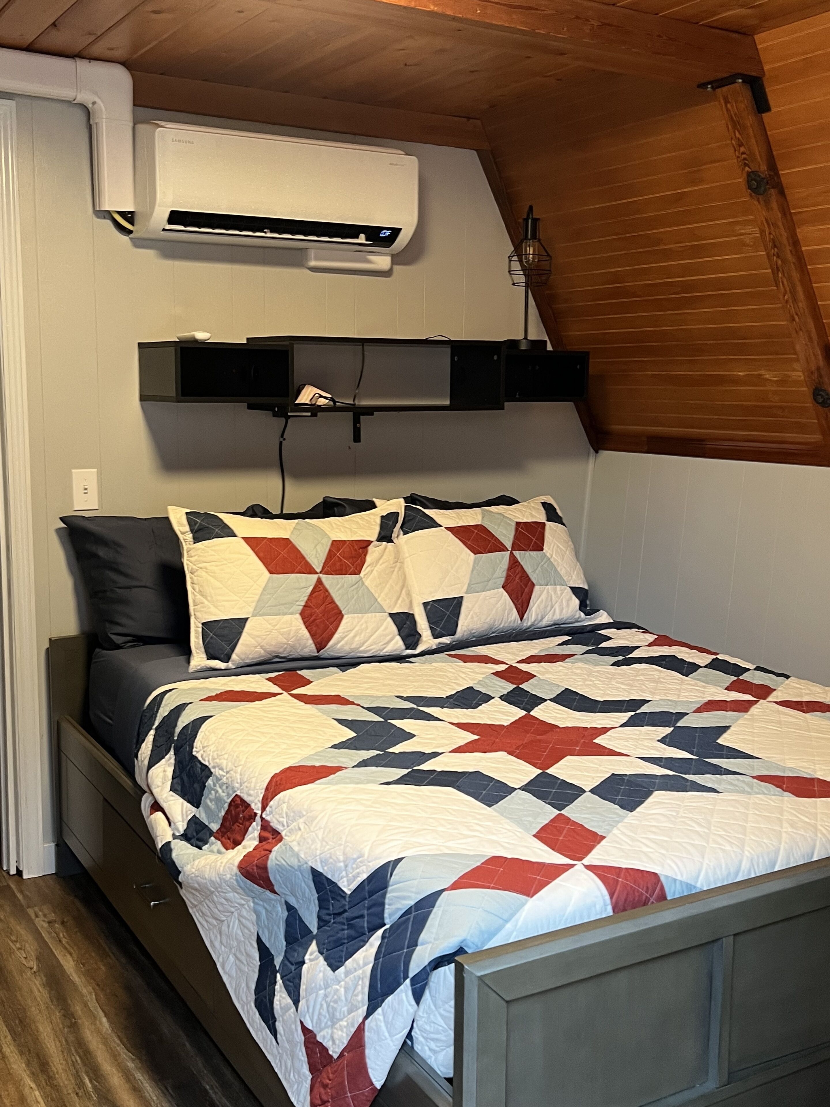 A bedroom with a bed, a wall-mounted air conditioner, and a wooden ceiling.