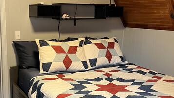 A bedroom with a bed, a wall-mounted air conditioner, and a wooden ceiling.