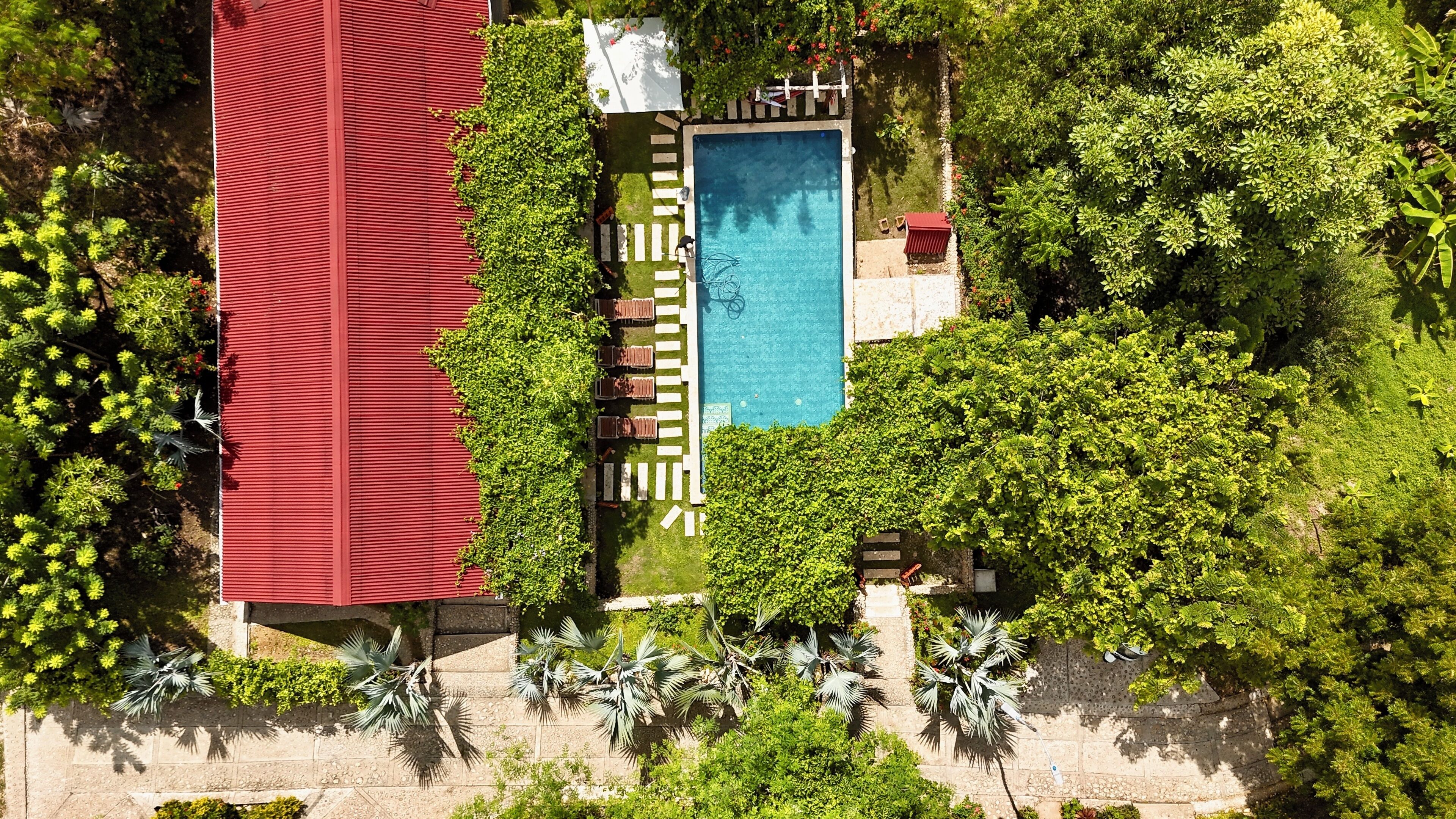 Vista aérea de una propiedad con piscina, rodeada de exuberante vegetación y un edificio con techo rojo.