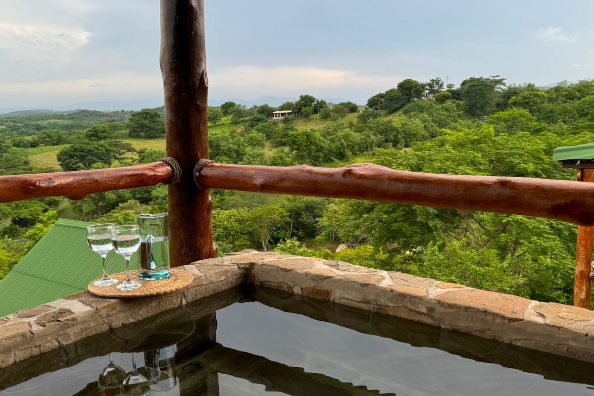 Une fontaine en pierre agrémentée d’une balustrade en bois, offrant une vue sur un paysage luxuriant.