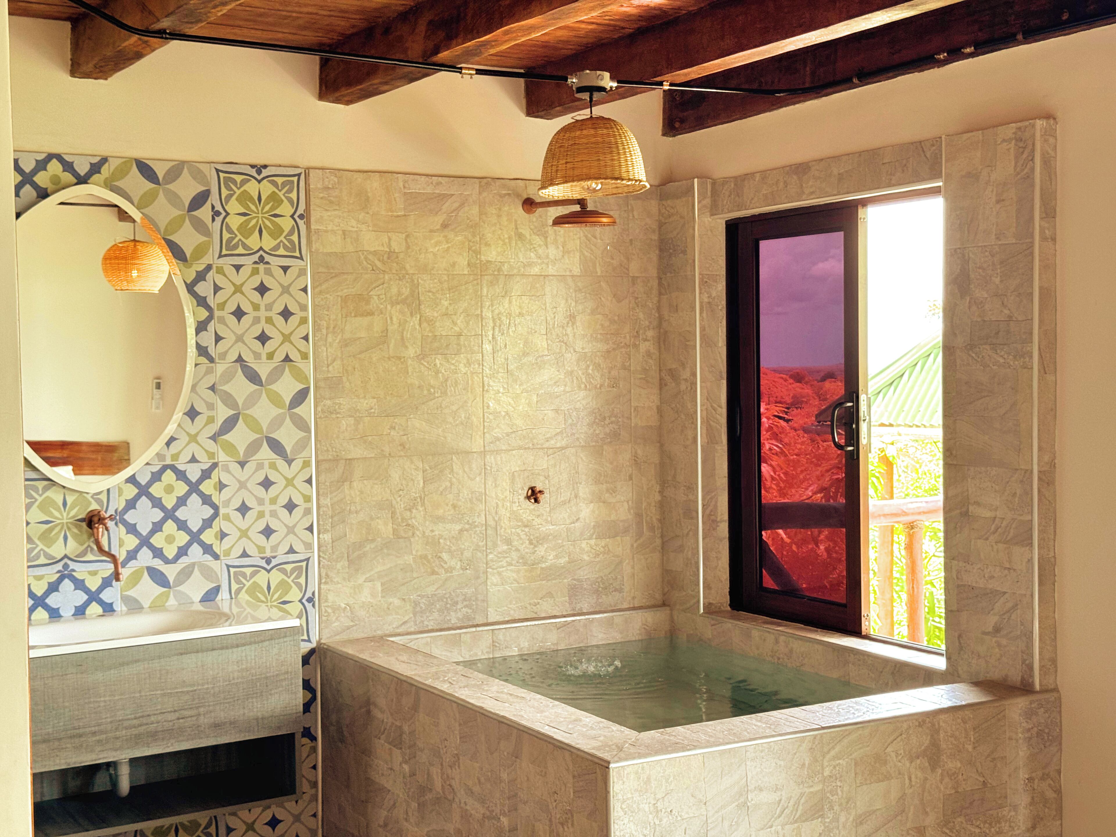A bathroom with a large mirror, a sink, a bathtub, and a window with a view of a red structure.