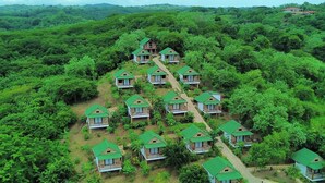 Un conjunto de pequeñas cabañas con techo verde rodeado de un bosque denso, con un edificio central más grande.