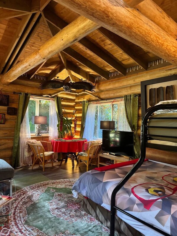 A cozy log cabin bedroom with a bed, a TV, a dining table, and a chair.