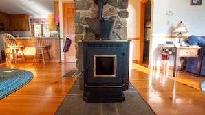 A cozy living room with a stone fireplace, wooden flooring, and a kitchen in the background. - Newfound Lake Hideaway Mooring included (Bristol)