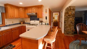 A kitchen with wooden cabinets, a central island, and a stone accent wall. - Newfound Lake Hideaway Mooring included (Bristol)