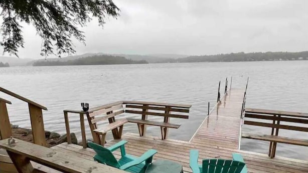 A wooden dock with benches and chairs extending over a body of water, leading to a distant shoreline. - Newfound Lake Hideaway Mooring included (Bristol)