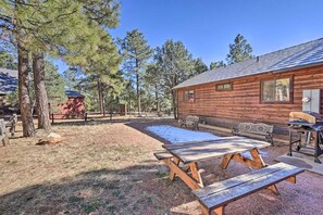 A rustic cabin with a wooden exterior, picnic tables, and benches in a wooded area.