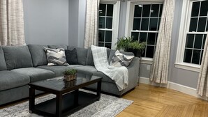 A modern living room with a grey sectional sofa, a dark wooden coffee table, and a patterned rug.