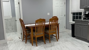 A dining area with a marble-tiled floor, a wooden table with four chairs, and a kitchen with grey cabinets and a coffee maker.