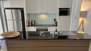 Une cuisine moderne dotée d’un plan de travail noir, d’appareils électroménagers en acier inoxydable et de lambris en bois.