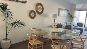 Un coin repas avec une table en verre entourée de chaises en osier, une plante en pot et des œuvres d’art décoratives accrochées au mur.