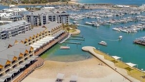 Un port de plaisance abritant de nombreux bateaux, une plage de sable et un hôtel doté de plusieurs balcons donnant sur l’eau.