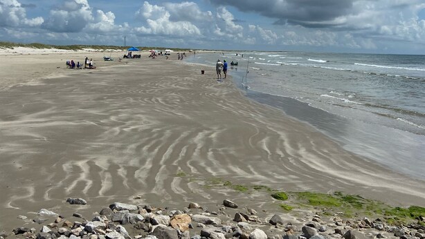 A beach with people, tents, and a rocky foreground.