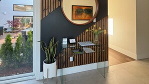 Een receptie met een wand van houten latten, een ronde spiegel, een potplant en een klein bureau met een bord.