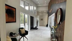 Een ruime hal met hoge plafonds, grote ramen en een modern ontwerp. Er zijn twee zithoeken met stoelen en tafels, en een decoratieve spiegel aan de muur.
