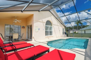 A covered outdoor swimming pool area with red lounge chairs, a ceiling fan, and a table with chairs. - Beautiful, sun-drenched 4 Bed 3 Bath Villa within The Sanctuary at West Haven (Davenport)