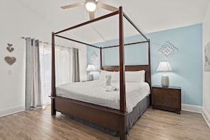 A four-poster bed with a wooden frame and white bedding, a nightstand with a lamp, and decorative wall art.