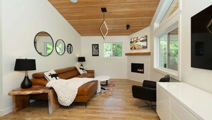 Een moderne woonkamer met een houten plafond, een open haard en een groot raam.