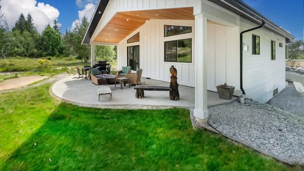 Een modern huis met een overdekt terras, tuinmeubilair en uitzicht op het omliggende landschap.