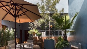 Un patio al aire libre con una mesa, sillas, un paraguas grande y varias plantas en macetas.