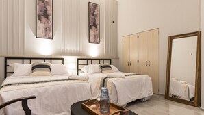 Habitación de hotel con dos camas, un aparador de madera, un espejo y una bandeja con una botella y un vaso.