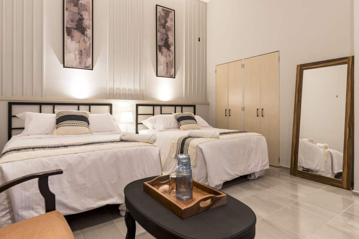 A hotel room with two beds, a wooden cabinet, a mirror, and a tray with a bottle and glass.
