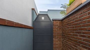 A narrow alleyway with a dark metal gate, brick walls, and a small planter with green foliage.