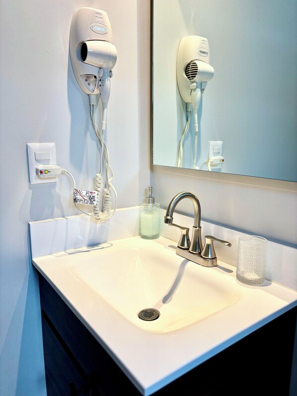 A bathroom with a white sink, a mirror, a hairdryer, and a bottle of hand soap. - Casa Murmullos (Guadalajara)
