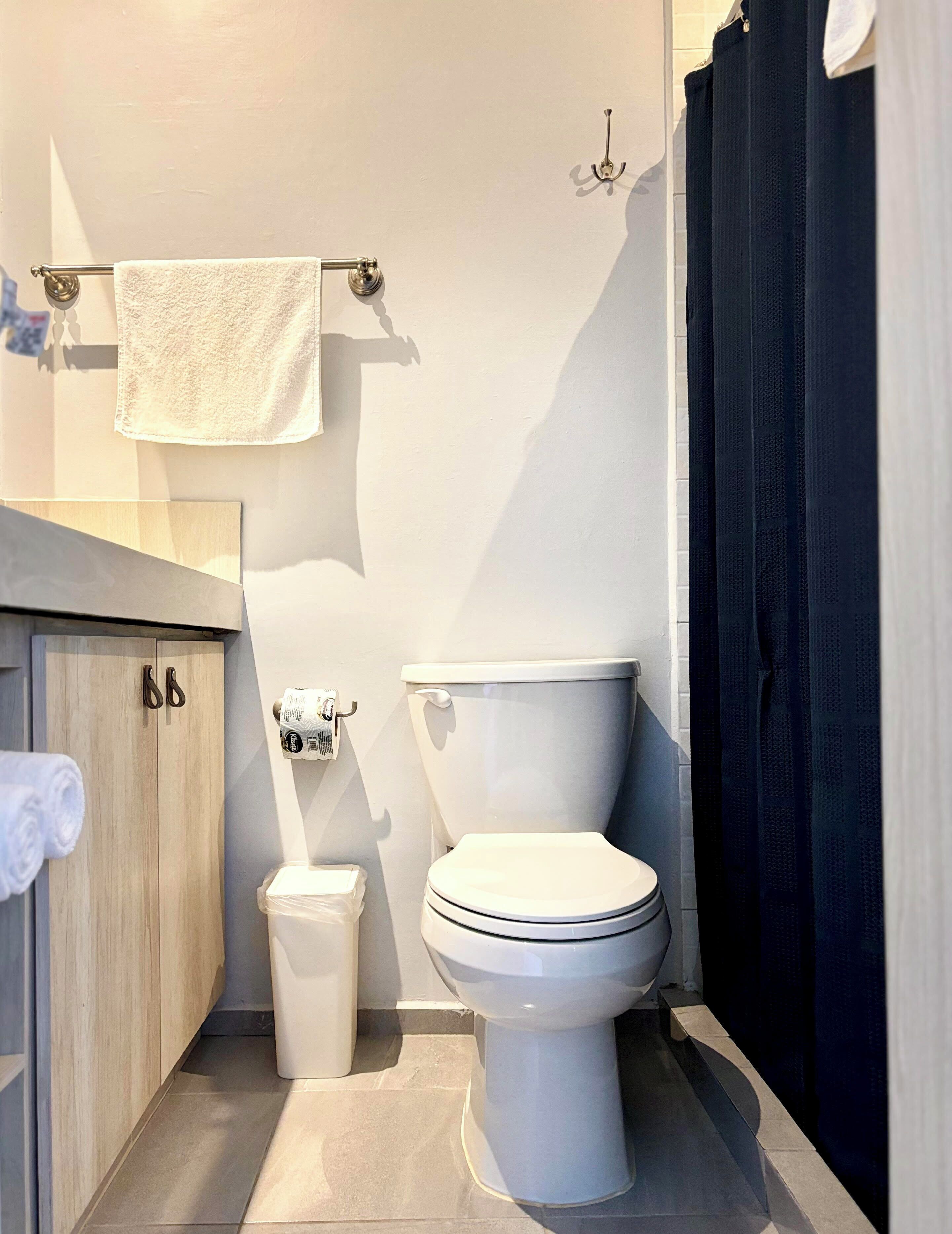 A compact bathroom with a toilet, a trash bin, a towel rack, and a shower curtain.