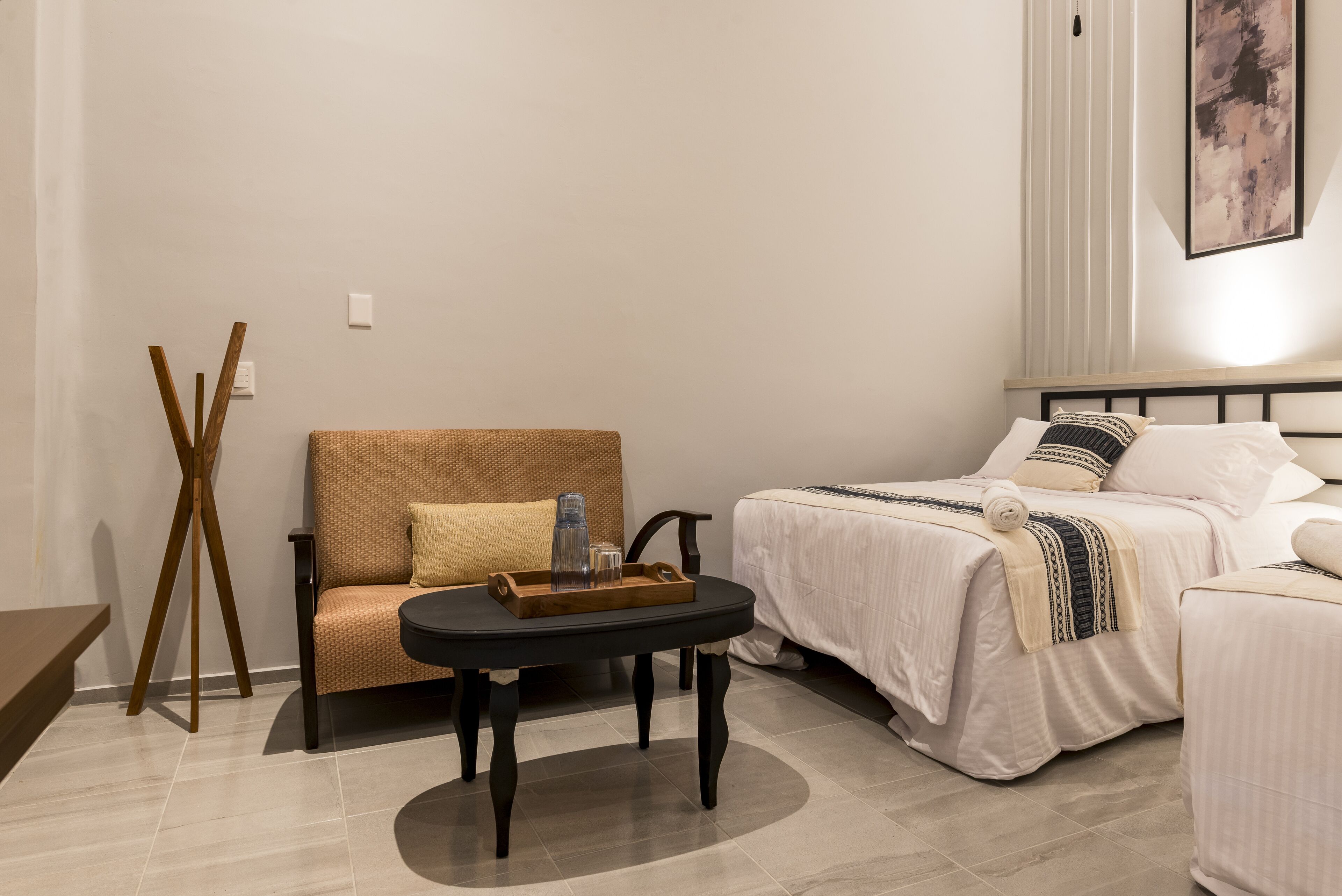 Une chambre d’hôtel avec un canapé, un lit, une petite table avec un plateau, et une œuvre d’art accrochée au mur.