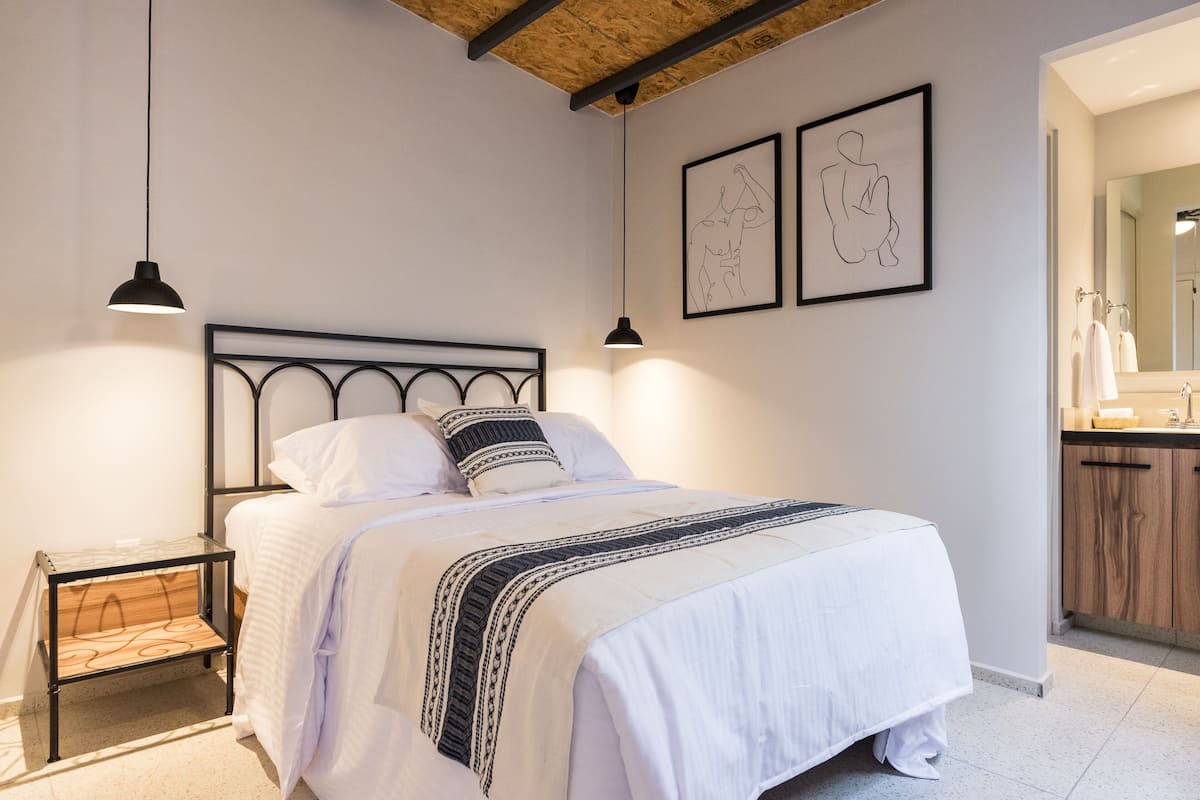A neatly made bed with a headboard, a bedside table, and two wall-mounted pendant lights.